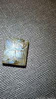 Rectangular natural labradorite gemstone carved with a four-leaf floral design, showing prominent blue flash under light on textured background.
