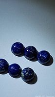 Close-up photo of six deep blue natural Lapis Lazuli round cabochon beads showing gold and white specks on smooth polished surface.