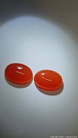 Matched pair of natural mandarin orange carnelian gemstones shown on a white background with clear polished surfaces and rich color saturation.