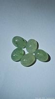 Five natural mint green oval cabochon kyanite gemstones on plain background.
