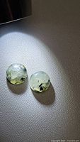 Photo showing two 10mm round cabochon moss agate gemstones with translucent pale green color and moss-like inclusions.