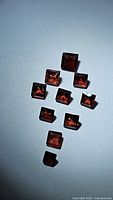 Eleven natural Mozambique garnet gemstones arranged on a light surface showing deep cherry red square cuts.