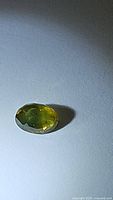 Oval cut natural sapphire showing green and yellow colors with facets visible, placed on neutral background.