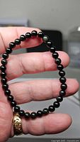 Full bracelet held in hand showing round black beads with uniform size and elastic cord.