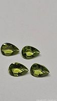 Four pear-cut natural peridot gemstones displayed on white background, showing consistent bright apple green color and clarity.