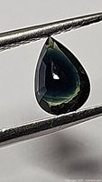Pear-cut tri-color sapphire in tweezers showing yellow zone near tip and green-blue gradient
