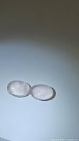 Pair of oval cabochon cut translucent light pink rose quartz stones placed side by side on a white surface with subtle shadowing.