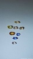 Top view of eight assorted pastel colored natural sapphires laid out on a plain surface.