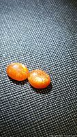 Close-up of two oval natural sunstone cabochons on black textured surface, showing bright orange color and glittery inclusions.
