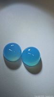 Two round, natural icy blue chalcedony cabochon gemstones about 10mm diameter on white background, showing smooth shiny surface and blue gradient.