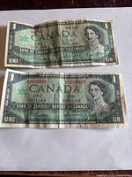 Front side of two Canadian Centennial one dollar bills, one with visible serial number and one without.