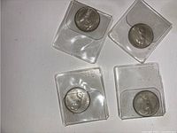 Four 1967 quarters each enclosed in square clear plastic holders, laid out on a surface, showing both coin faces.