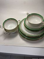 Full set of Aynsley fine bone china including stacked soup cups, saucers, and plates showing green and gold detailed trim