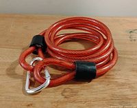 Red bicycle security chain coiled with visible black protective loop covers and attached silver carabiner on wooden surface.