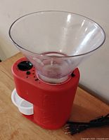 Red Bodum electric coffee grinder with clear plastic bean hopper on top, white grounds container, control dial, and power cord visible.