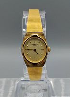 Front view of the Caravelle by Bulova women's gold tone quartz dress watch on a clear display stand, showing dial and bracelet detail.