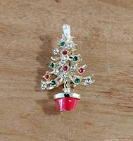 Front view of the Christmas tree brooch showing gold-tone metal with colored rhinestones and red enamel tree pot.