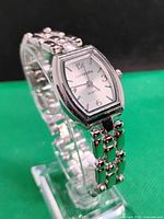 Silver-tone ladies Concepts dress watch with rectangular curved case and multi-link bracelet style band. Silver dial with Arabic numerals and quartz movement.