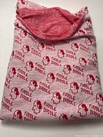 Photo of a folded double knit tubular fabric featuring red 'Fuddle Duddle' text and graphic patterns with a red reverse side visible.