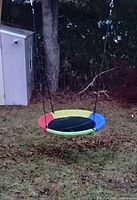 Full view of the saucer style canvas swing hanging outdoors showing multicolor canvas seat.