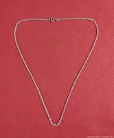 Full view of delicate sterling silver chain necklace, laid out flat on red textured background, showing the chain style and length.