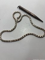 Silver chain necklace laid out with pencil-shaped pendant attached.