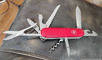Red Victorinox Swiss Army multi-tool knife with multiple blades and tools extended on a dark leather surface.