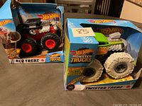 Two Hot Wheels Monster Trucks in damaged packaging: Rev Tredz (black) and Twisted Tredz (green)