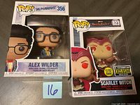 Two boxed Marvel Funko POP! figures, Alex Wilder #356 and Scarlet Witch #823, shown side by side on a table with a small blue note with number '16'.