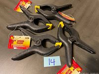 Four new KC 2-inch spring clamps arranged on a dark surface, showing front view with labels attached.