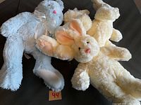 Four stuffed animal bunnies laid out on a surface in pastel colors including white, cream, and light gray. Visible are the soft fabric texture, floppy ears, and sewn facial features.