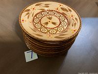 Stack of eight small decorative plates showing front face with floral and leaf pattern in brown and orange colors.
