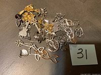 Mixed metal charms including keys, mermaid, bird, hearts, hand, and other symbols spread on a flat surface with sticker number 31.