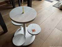 Photo showing entire white-washed wooden multi-tier display stand on wooden floor, highlighting circular tiers and central support.