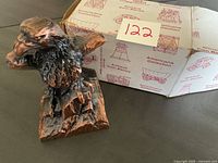 Front and side views of brass eagle bank with detailed feathering and rock base, alongside original packaging box labeled 'Americana Collection'.