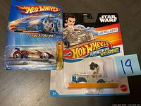 Image showing one Hot Wheels Track Aces die-cast car in original packaging and one Hot Wheels Star Wars Racer Verse character vehicle, both still sealed.