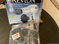 Photo showing hair dryer and diffuser attachment in plastic bag with damaged box in background