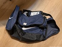 Full view of the navy and black Nike duffle bag with white logo and shoulder strap.