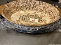 Oval ceramic casserole dish with integrated side handles. Floral pattern inside and around rim with brown, beige, and cream colors.