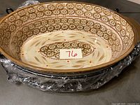 Top inside view of the oval ceramic casserole dish showing intricate floral and leaf designs in brown and cream, with orange accent dots.