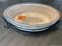Side angle showing ceramic oval casserole dish with floral pattern inside, resting on black metal stand, photographed with orange label on dish