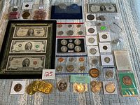 Full view of the currency and coin collection laid out on a fabric surface including framed vintage banknotes, silver certificate, assorted coins, medallions and tokens.