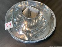 Two unopened Pampered Chef cake pans: one heart-shaped, one tube-shaped with decorative base. Both sealed with packaging and instruction insert inside.