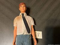 Full body photo of vintage 1968 Ken doll wearing white shirt, black tie, and blue pants.