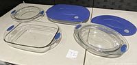 Four Anchor Hocking glass casserole dishes with two blue plastic lids and one clear glass lid displayed on table