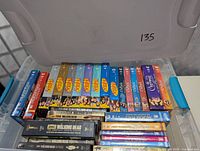 Top view of assorted DVD box sets in a plastic storage bin showing titles including Seinfeld, The Walking Dead, Melrose Place, and Charmed.