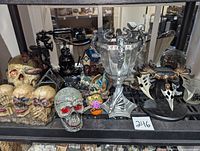 Shelf displaying assorted Halloween-themed decorative items including skulls, dragon statues, fantasy dagger, cup, and haunted station miniatures.