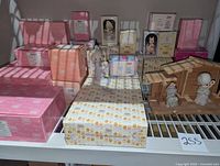 Photo of assorted Precious Moments figurines in boxes and some displayed, including nativity stable on shelf.