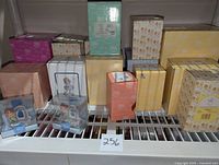 Photo showing multiple Precious Moments figurine boxes and a couple of figurines in plastic cases arranged on a white grid surface.