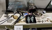 Assorted fashion jewelry items displayed on a table, including bolo tie, earrings, rings, and pendants. Photo shows a variety of metal and stone materials with some pieces in plastic bags.